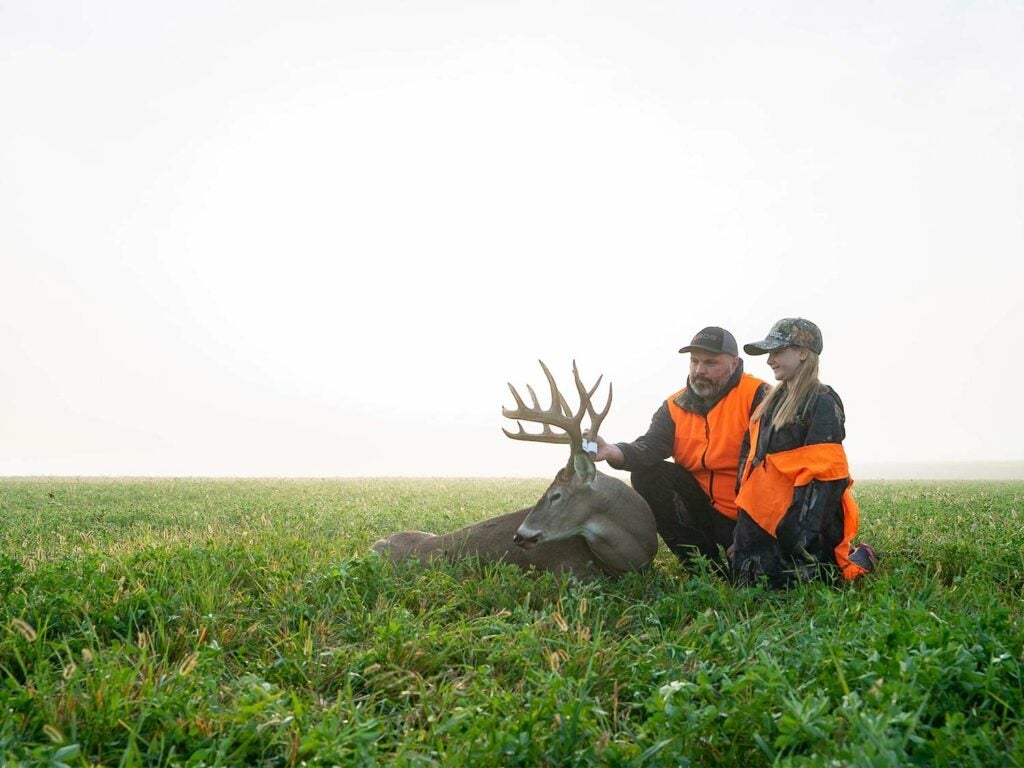 A young girl and her stepfather admire the buck taken in a large open field.