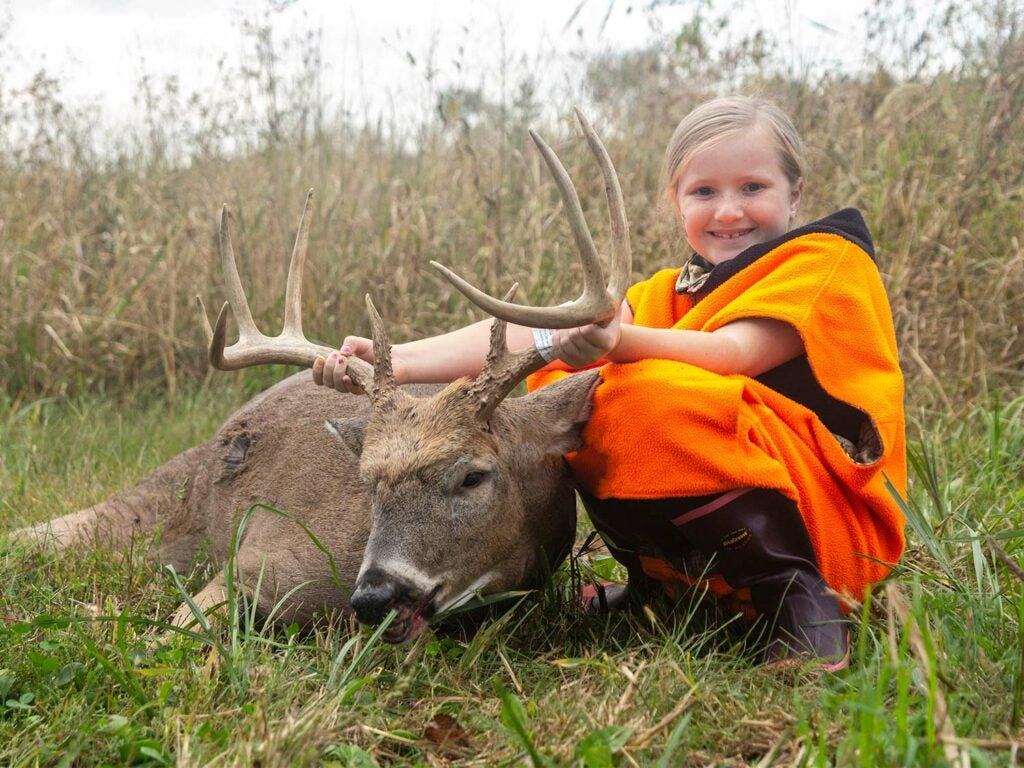 A young girl holds up the antlers of a deers head.