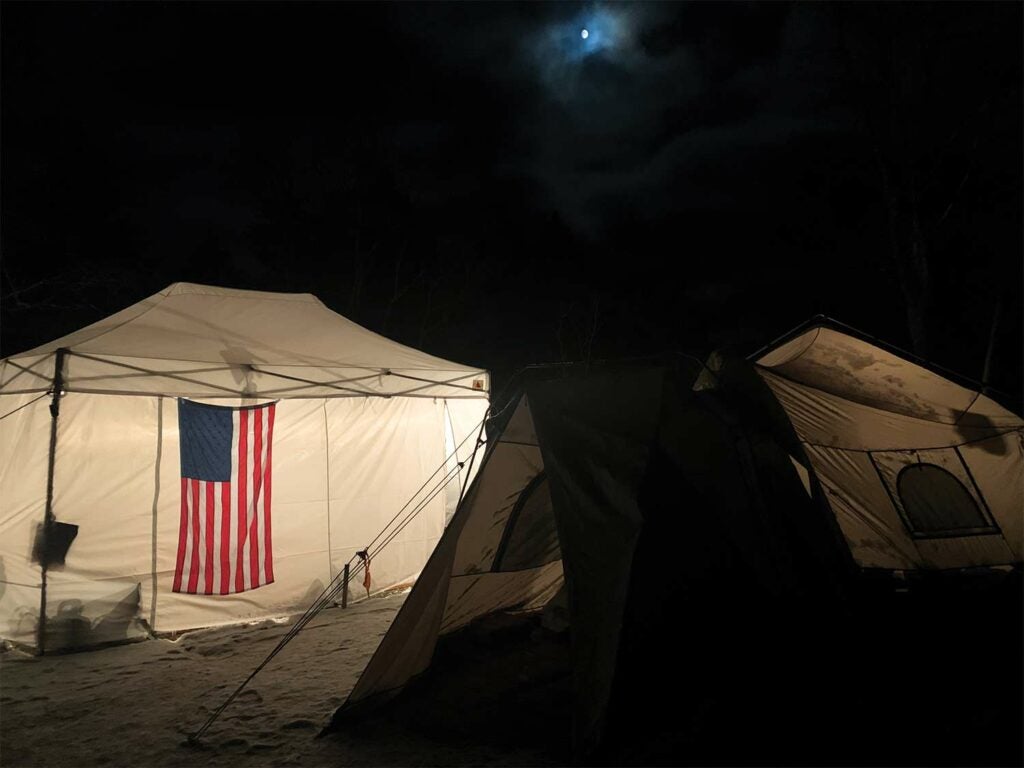 An American flag hanging on the outside of a white camping tent at night.