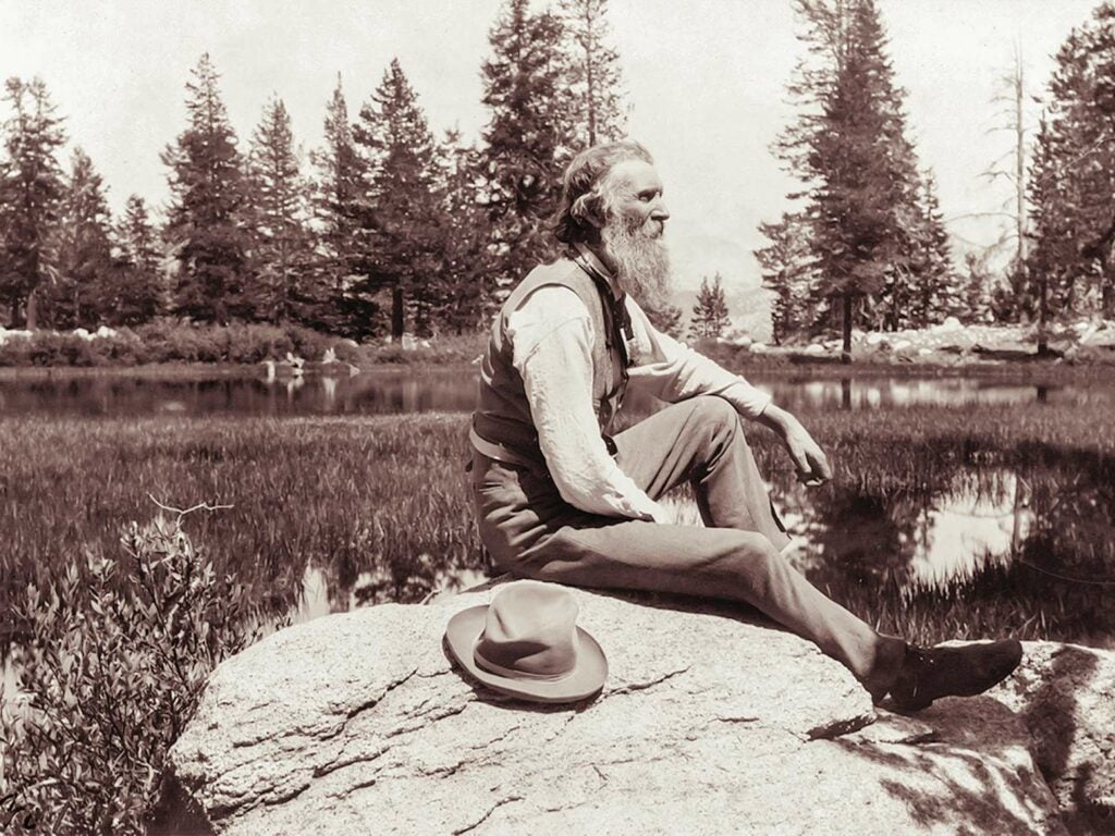 John Muir sitting on a rock.