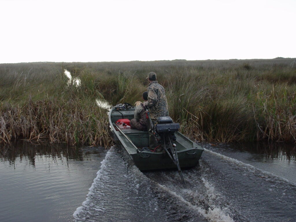A hunter drives a jon boat with a long-tail engine.