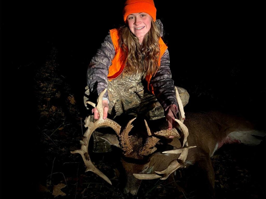 A young girl poses with a whitetail deer and holds its head by its antlers.