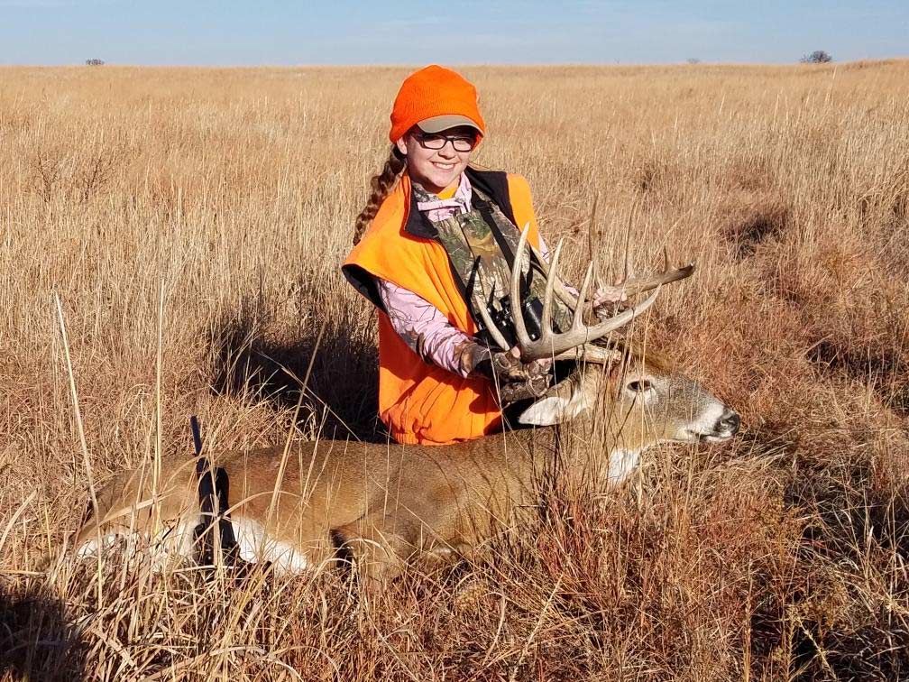 A young girl poses next to a whitetail buck.