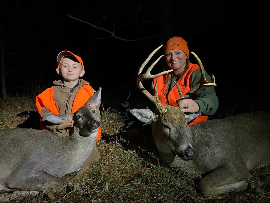 A woman and young boy kneel behind dropped deer.