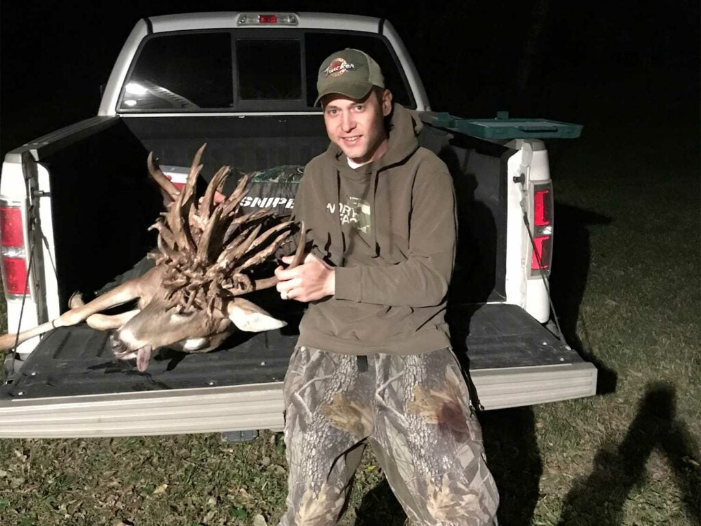 A hunter standing next to a large whitetail buck with a nontypical antler spread.