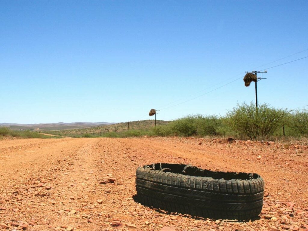 A blown out tire on the side of a dirt road.