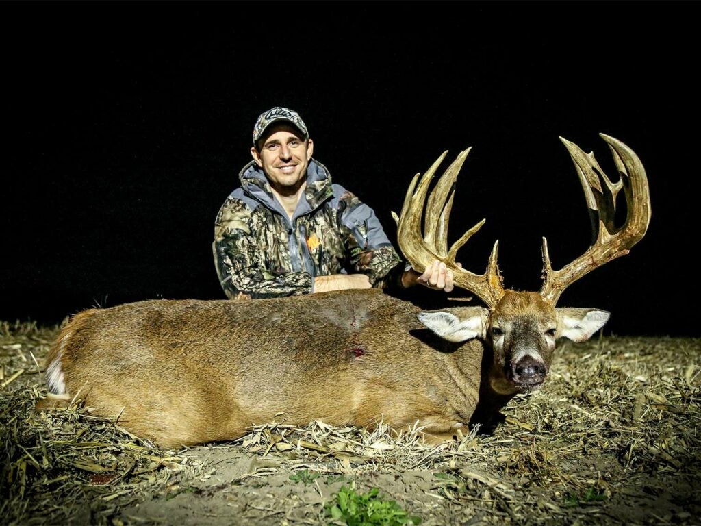 A hunter kneels behind a large whitetail buck.