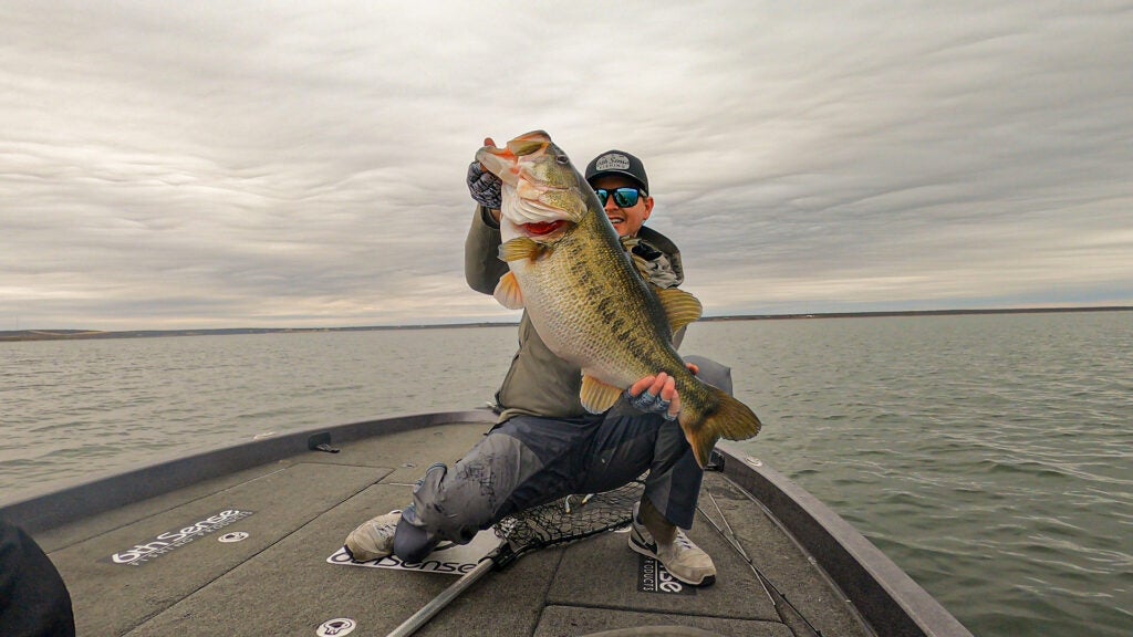Man on boat in lake holding big largemouth bass.